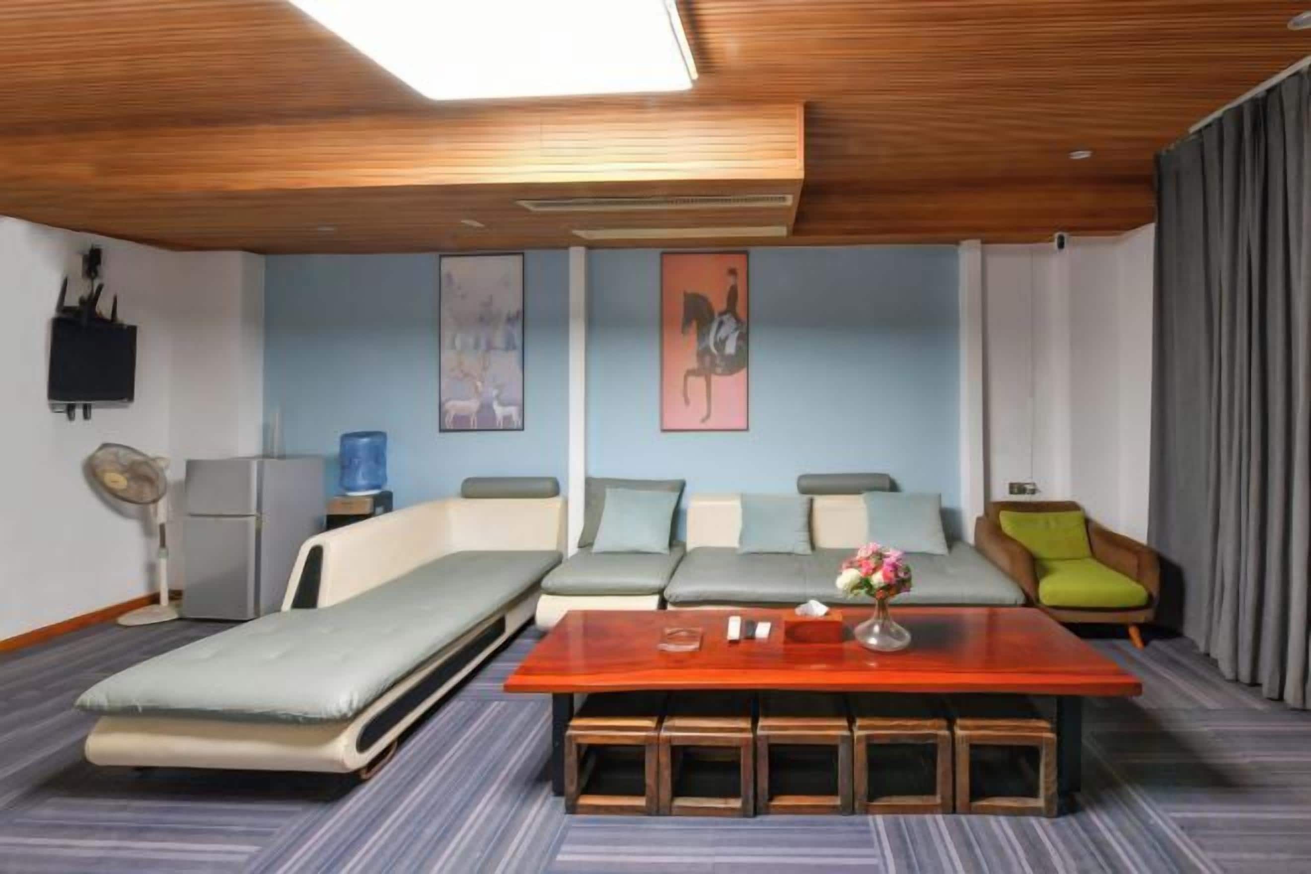 A room with a bed, a sofa, a table with a vase, and a fan.