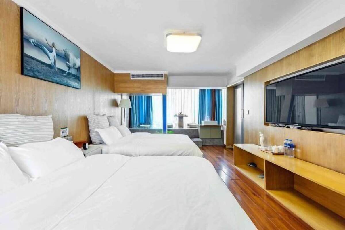 Une chambre d’hôtel avec deux lits, une télévision, un tableau et une vue sur l’extérieur.