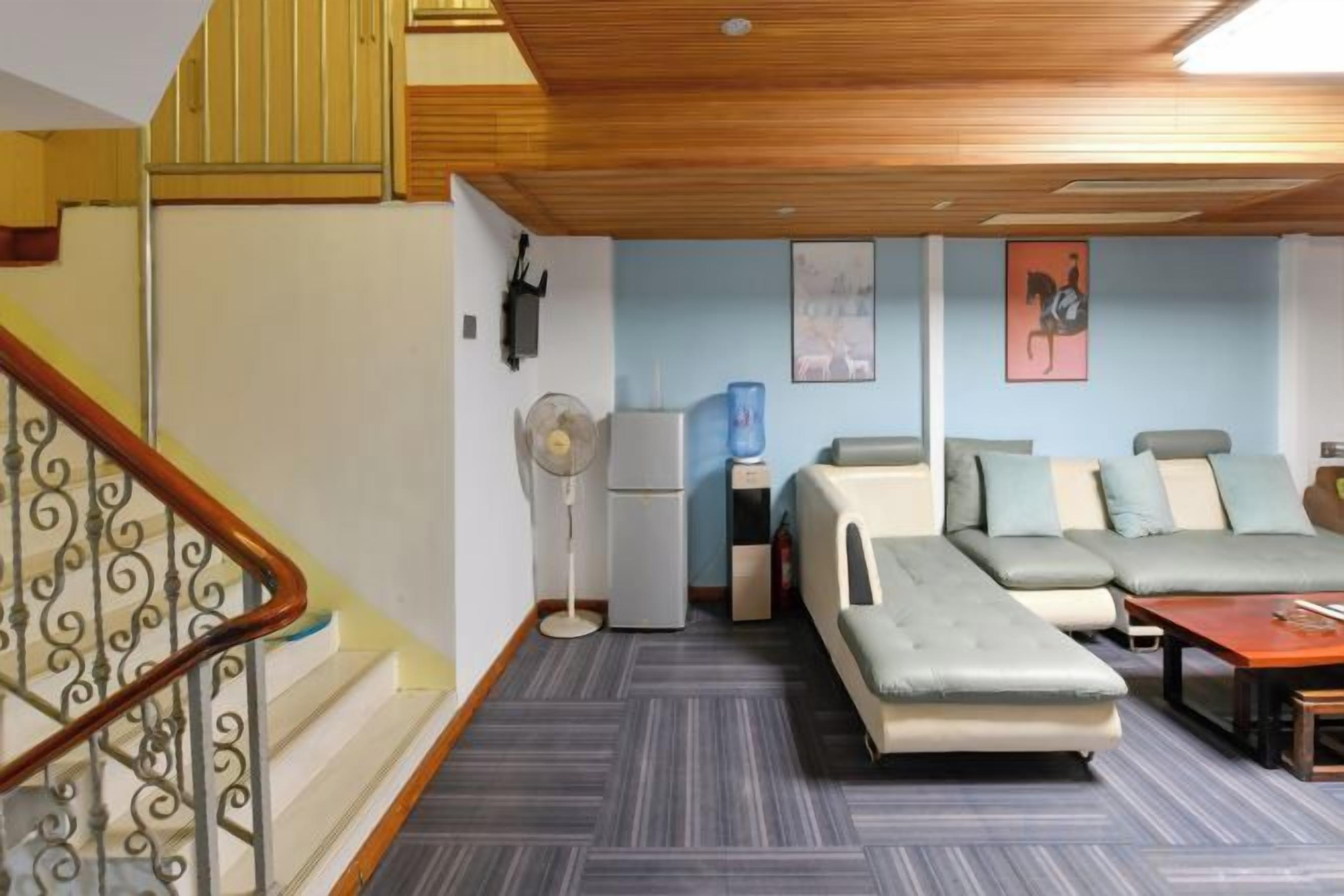 A room with a sofa, a small table, a standing fan, and a refrigerator.