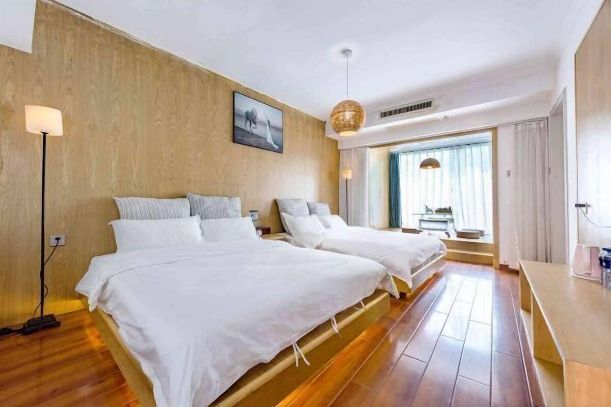 Une chambre d’hôtel avec deux lits, un plancher en bois, une grande fenêtre avec des rideaux et un tableau accroché au mur.