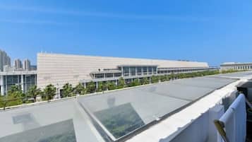 A modern building with a flat roof and large glass windows, surrounded by greenery and other buildings.