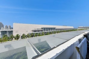 Un edificio moderno con techo plano y amplias ventanas de vidrio, rodeado de vegetación y otros edificios.