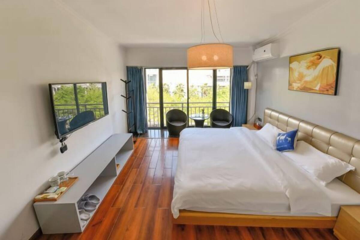 Une chambre d’hôtel avec un grand lit, un téléviseur fixé au mur, un balcon avec des chaises et un tableau au mur.