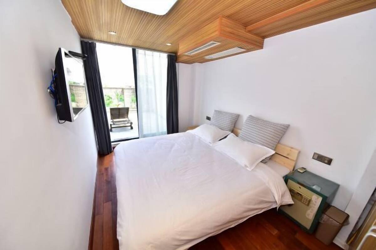 Une chambre à coucher avec un lit, une table de chevet, une télévision et une fenêtre avec des rideaux.