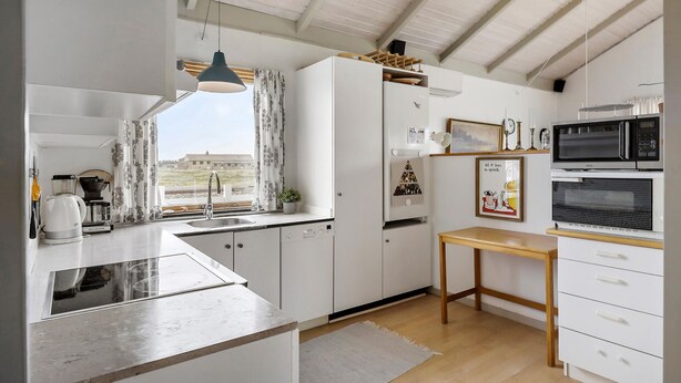 Una cocina moderna con un amplio ventanal, armarios blancos, una mesa de madera y un microondas.