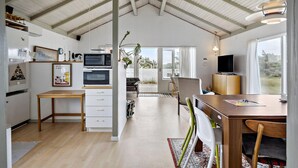 Una habitación amplia con techo alto, zona de comedor con mesa y sillas, cocina equipada y un ventanal con vistas al exterior.