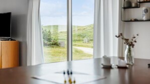 Una habitación con un gran ventanal, un escritorio de madera, un televisor y un jarrón con flores secas.