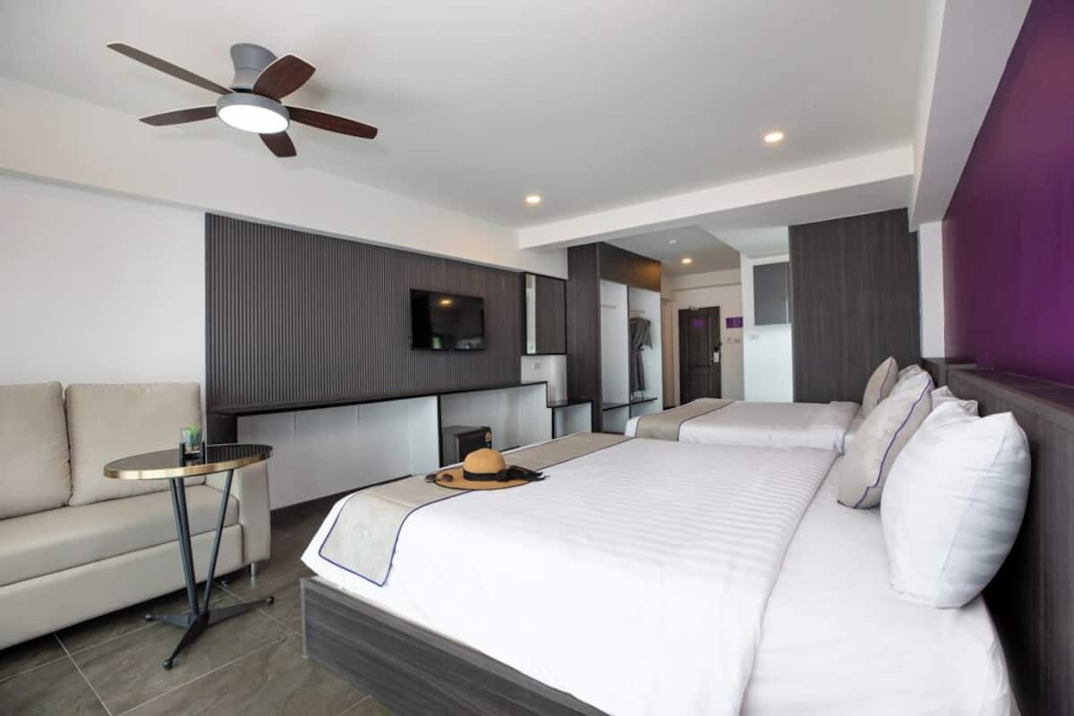 Una habitación de hotel moderna con una cama grande, un pequeño sofá, una mesa redonda, un ventilador de techo y un televisor.