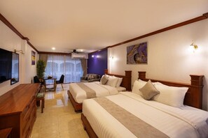 Ein Hotelzimmer mit zwei Betten, einem Schreibtisch und einem Stuhl. Es gibt ein Fenster mit Vorhängen, ein Bild an der Wand und einen Deckenventilator.