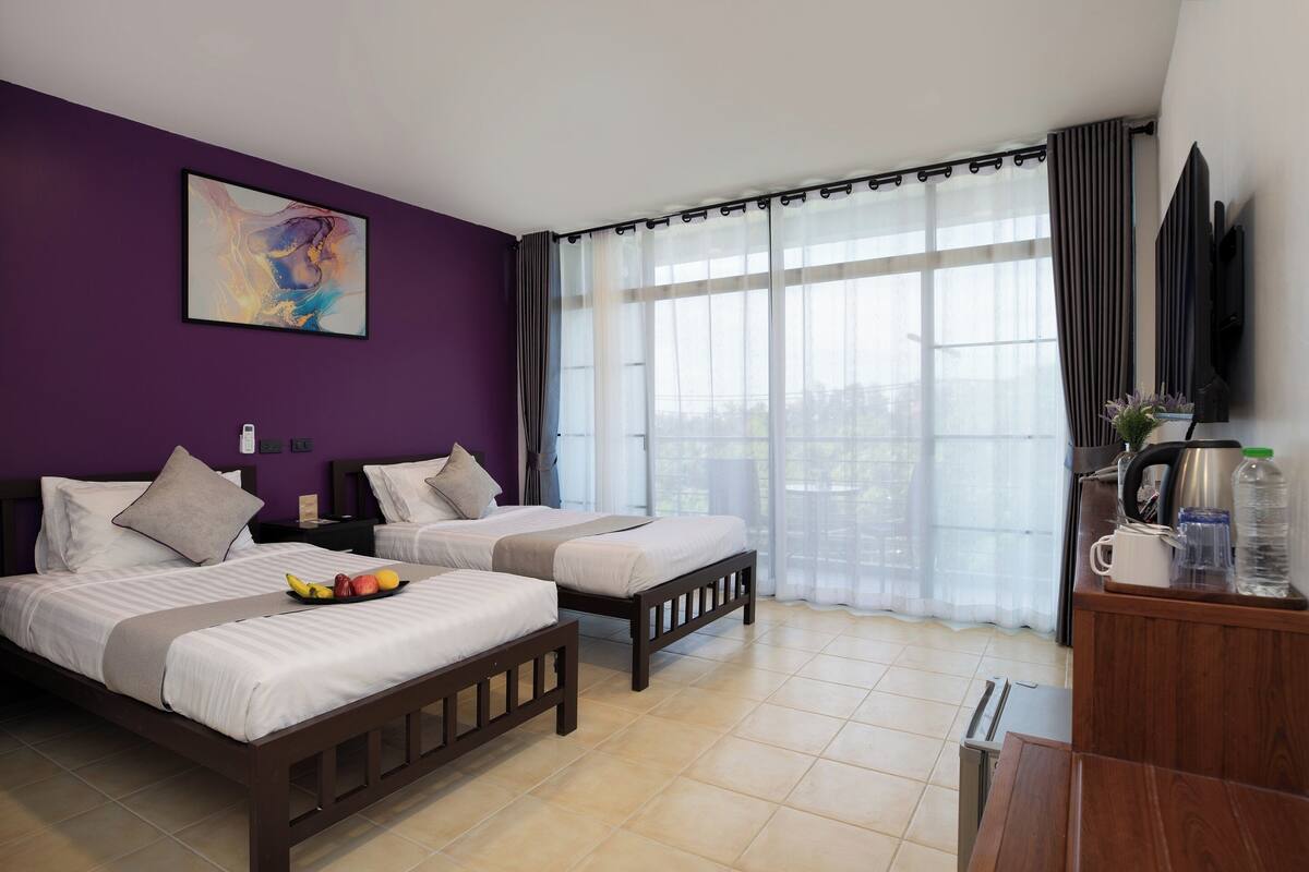 Habitación de hotel con dos camas, un ventanal con cortinas, un cuadro en la pared y una zona de kitchenette.