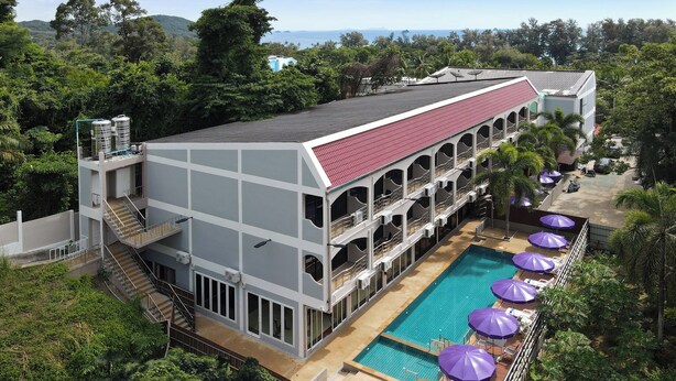 Un hotel de varios pisos con piscina, sombrillas exteriores y techo rojo.