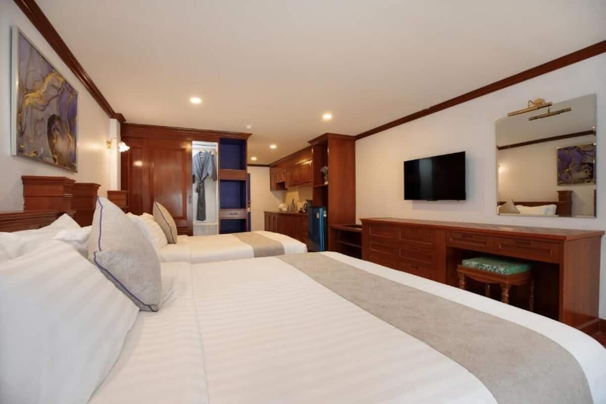 Habitación de hotel con dos camas, televisión, escritorio y baño a la vista a través de una puerta abierta.