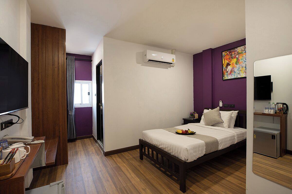 Una habitación de hotel con cama, escritorio, televisor, aire acondicionado y un refrigerador pequeño.