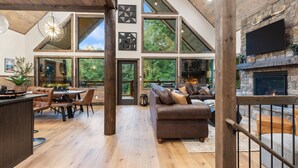Amplia sala de estar con chimenea, pisos de madera y ventanas grandes que ofrecen vistas al exterior.