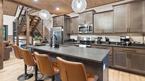 Una cocina moderna con una isla central, taburetes de bar, electrodomésticos de acero inoxidable y una escalera de madera.