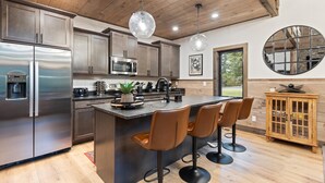 Una cocina moderna con electrodomésticos de acero inoxidable, una isla central con taburetes de bar, armarios de madera e iluminación colgante.
