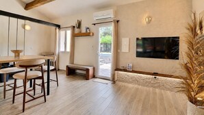 A modern interior with a wooden dining table, chairs, a bench, a TV mounted on the wall, and an air conditioning unit. - Le 522 – Nature Retreat & Jacuzzi (Ventabren)