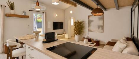 Una cocina moderna con una isla central, luces colgantes, un televisor de pantalla plana y un comedor con taburetes de bar.