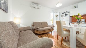 A modern living room with a sofa, a chair, and a dining table with chairs. There is a kitchen area with appliances and a small plant on the counter. - 2 bedroom lovely apartment in Povljana (Povljana)
