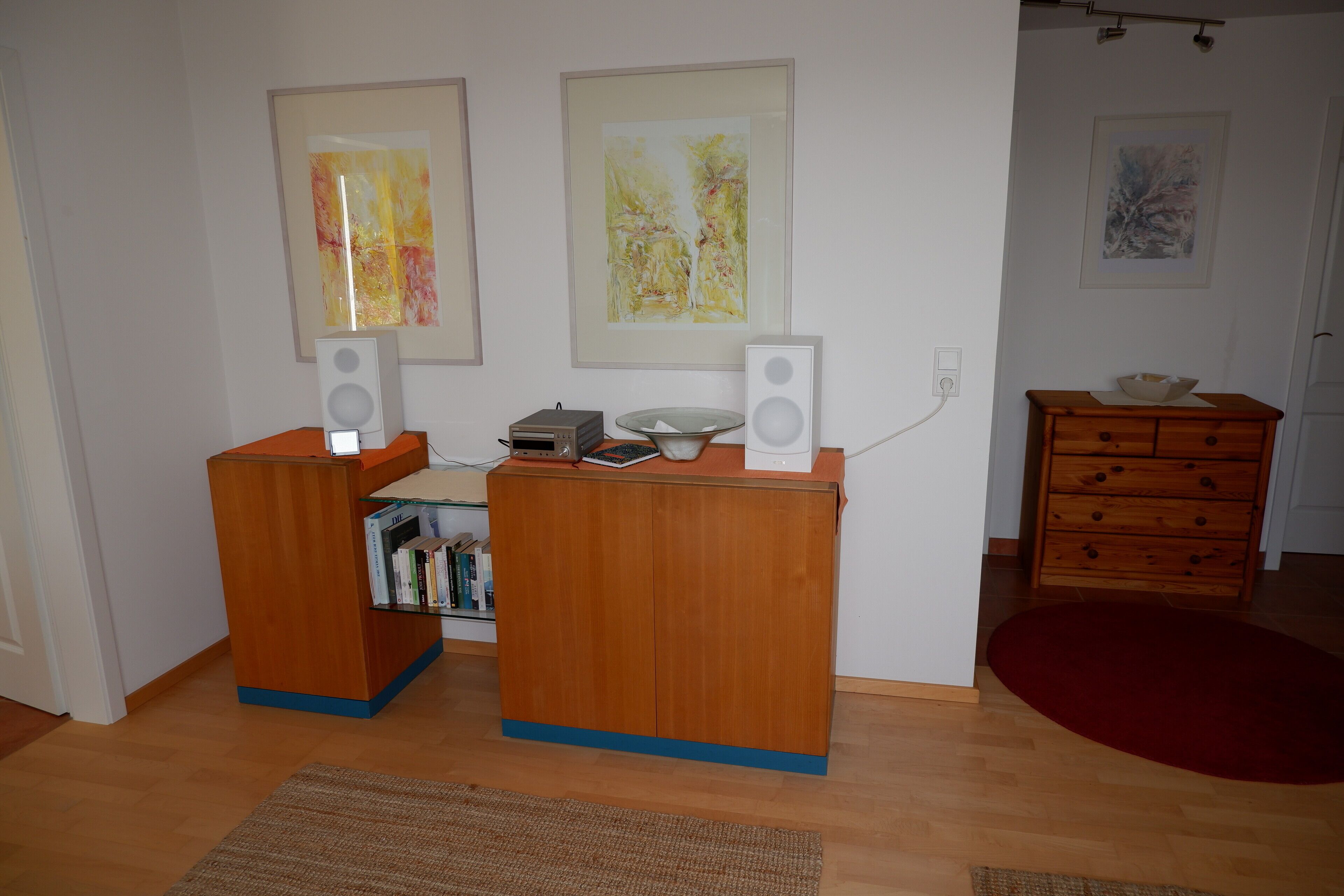 Ein Zimmer mit zwei Holztischen, einem Bücherregal und gerahmten abstrakten Gemälden an der Wand.