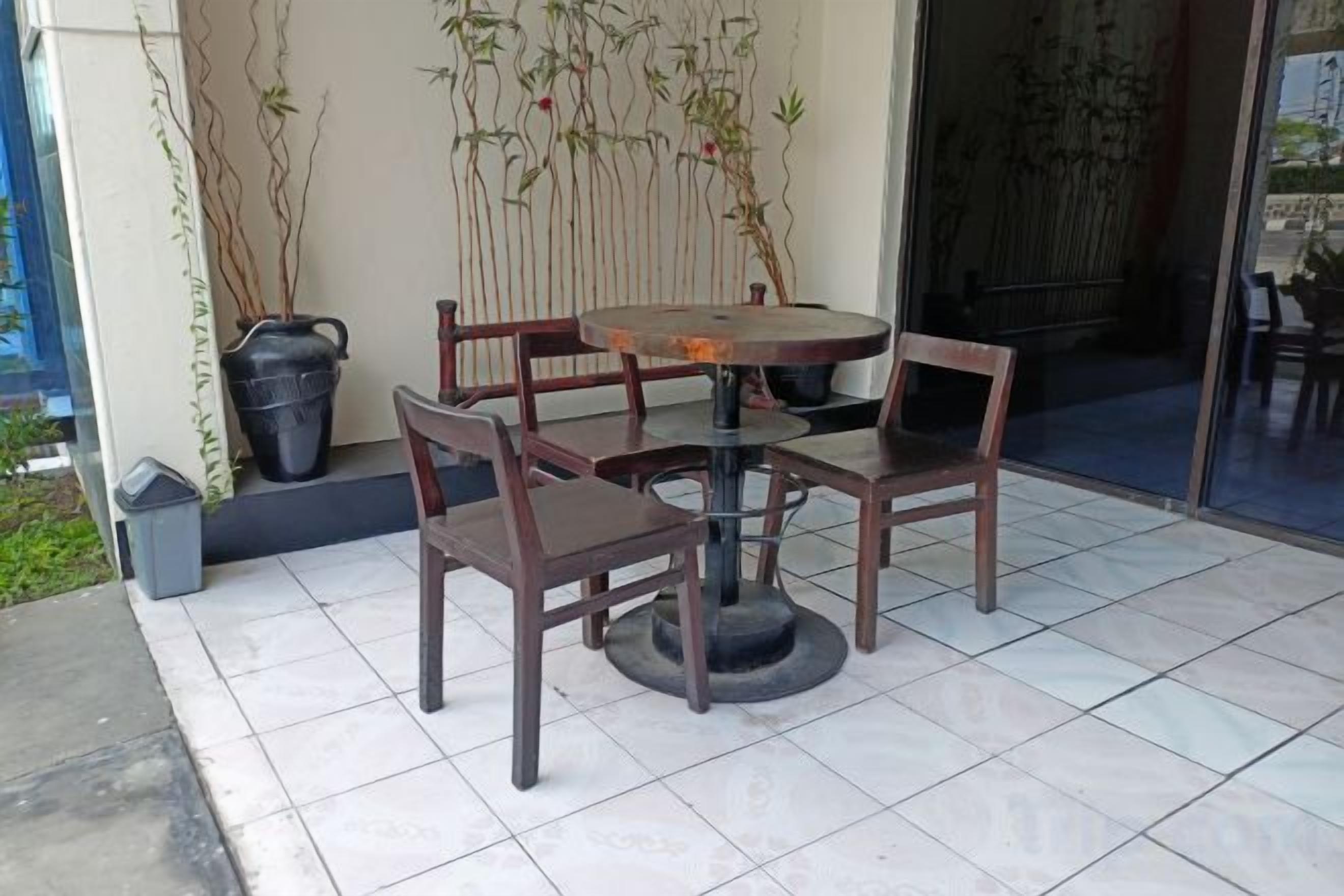 Eine Terrasse mit einem runden Tisch, vier Stühlen, einem Blumentopf und einem Mülleimer.