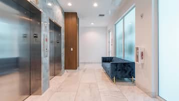 Un área de ascensores moderna con dos ascensores, un revestimiento de paneles de madera, un sofá azul y un extintor.