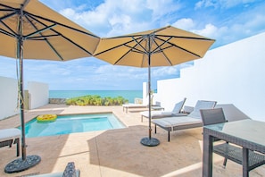 A poolside area with lounge chairs and umbrellas, a clear view of the sea, and a stone wall. - Oceanfront with Beach Access & Private Pool 3BR (Nassau)