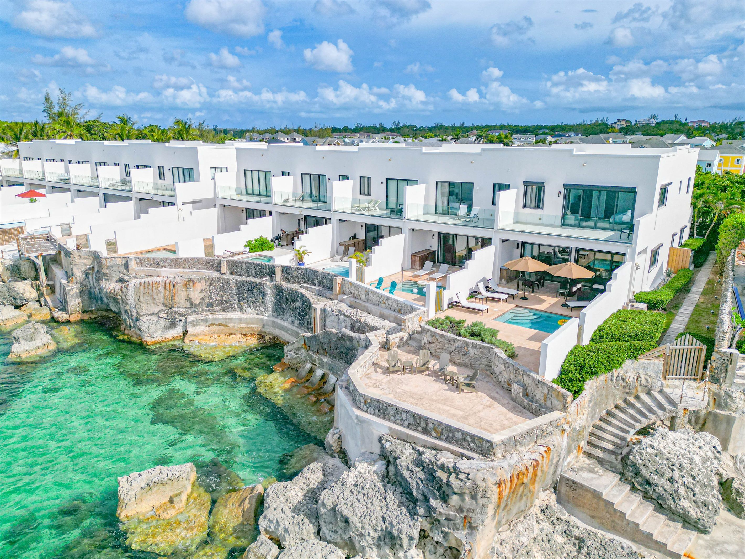 A modern resort with a pool surrounded by stone walls, a covered outdoor seating area, and a view of the ocean.