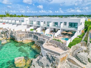 Een modern resort met een zwembad, omringd door stenen muren, een overdekt terras en uitzicht op de oceaan.