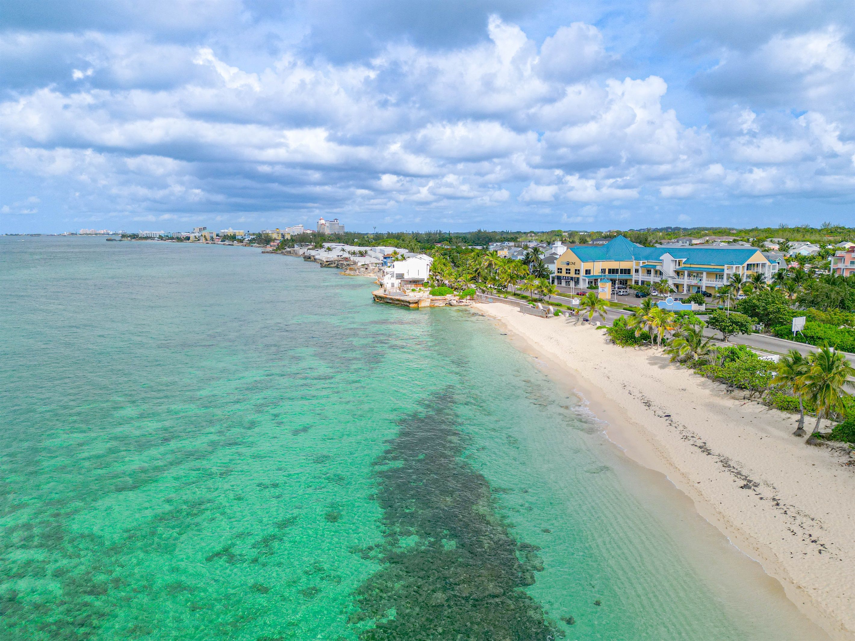 A coastal hotel with a beach view, clear turquoise water, and a row of palm trees.