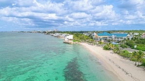 A coastal hotel with a beach view, clear turquoise waters, and a row of palm trees. - 3 BR Oceanfront Beach House with Private Pool Gated Community Staircase to Ocean (Nassau)