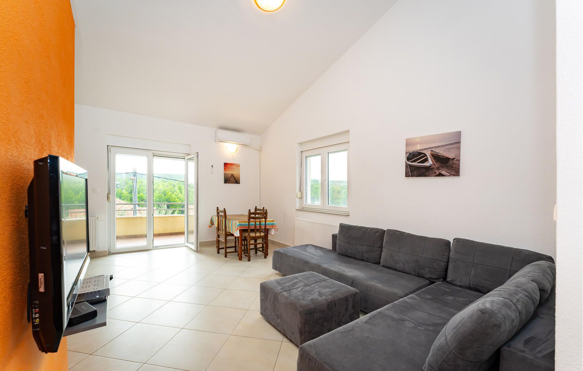 A modern living room with a grey sofa, a dining table with chairs, and a balcony with a view.