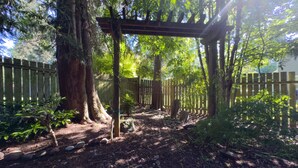 Une zone boisée agrémentée d’une pergola en bois, d’une clôture en bois et d’un sentier bordé de pierres.