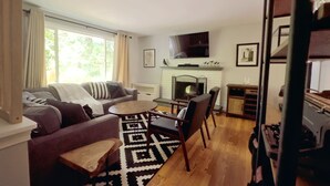 Un salon comprenant un canapé, des fauteuils, une table basse, une cheminée et un téléviseur.