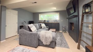 Un salon avec un canapé gris, une table basse, un tapis, un téléviseur et une cheminée.