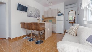 Un espace de vie compact comprenant un coin cuisine, un coin repas avec des tabourets de bar, un canapé blanc et un miroir.