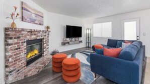 Ein Wohnzimmer mit Kamin aus Ziegelsteinen, einem blauen Sofa und einem Flachbildfernseher.