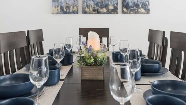 Ein Esstisch ist gedeckt mit blauen Tellern, Weingläsern und einer Mittelstück-Dekoration mit Blumen und einer Kerze.