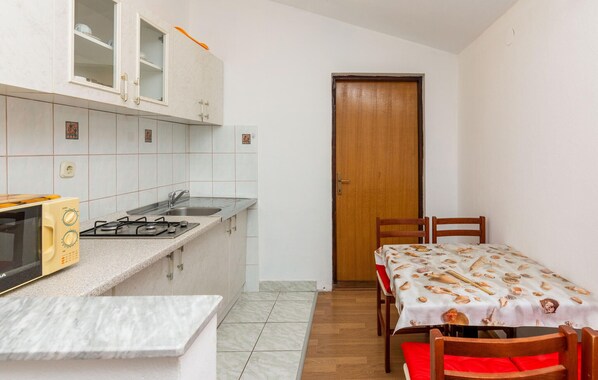 A compact kitchen with a gas stove, sink, and cabinets. There's a dining table with a tablecloth and chairs.