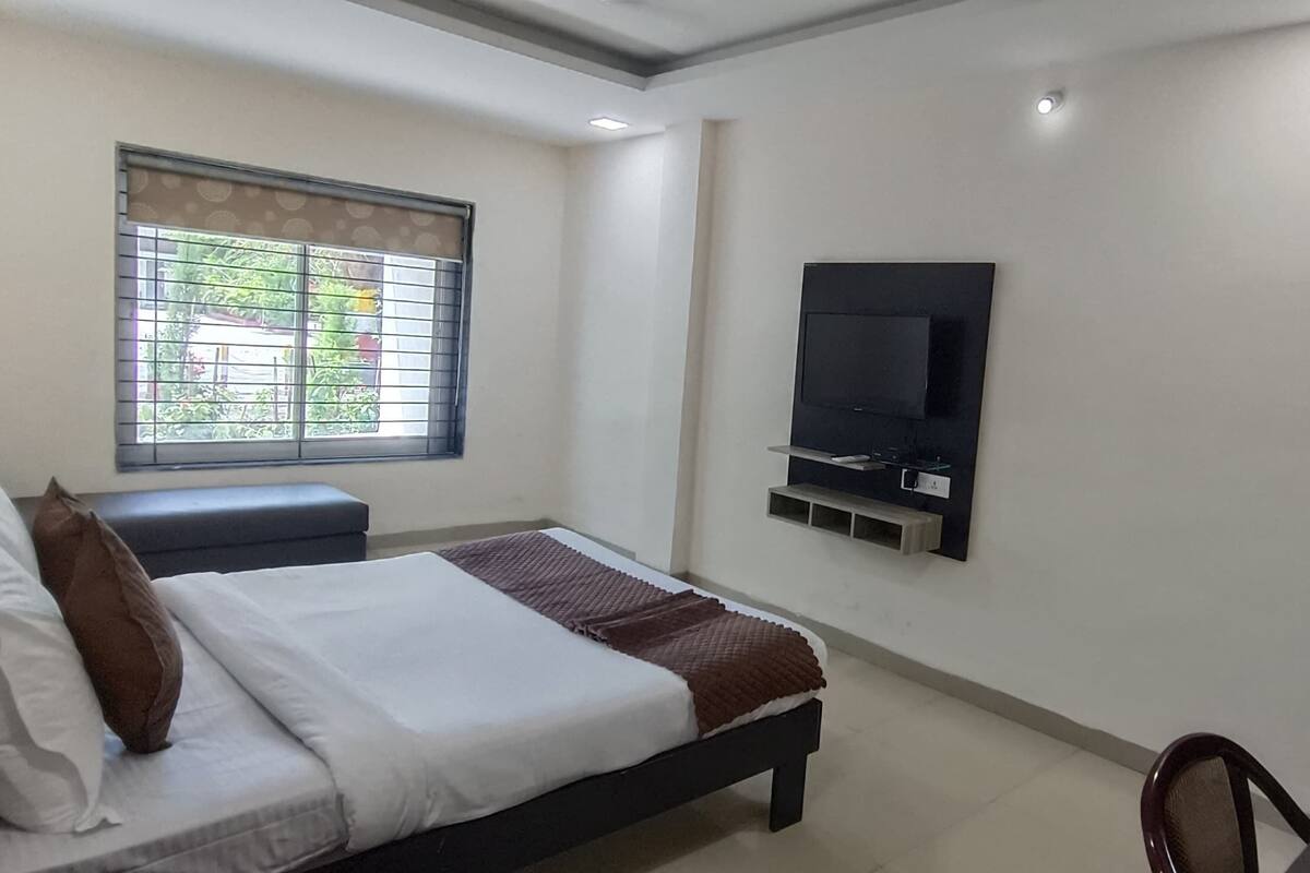 Un dormitorio con una cama, un televisor montado en la pared, una ventana con persianas y una puerta.