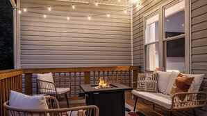 Un espace extérieur aménagé avec des meubles de jardin en osier, une table, un foyer et des guirlandes lumineuses.