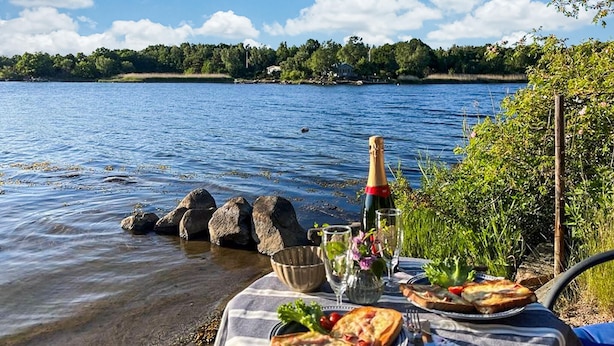 A lakeside picnic setup with a bottle of champagne, a glass, a bowl, and plates of food. - Nice home in Ronneby with WiFi (Ronneby)