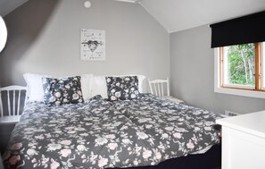 A bedroom with a bed, white headboard, floral bedding, a window with a view of greenery, and a wall-mounted artwork. - Nice home in Ronneby with WiFi (Ronneby)