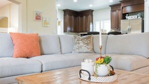 A living room with a grey sofa, a wooden coffee table with a tray, and a kitchen in the background.