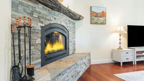 A stone fireplace with a fire, a TV on a stand, and a painting on the wall.