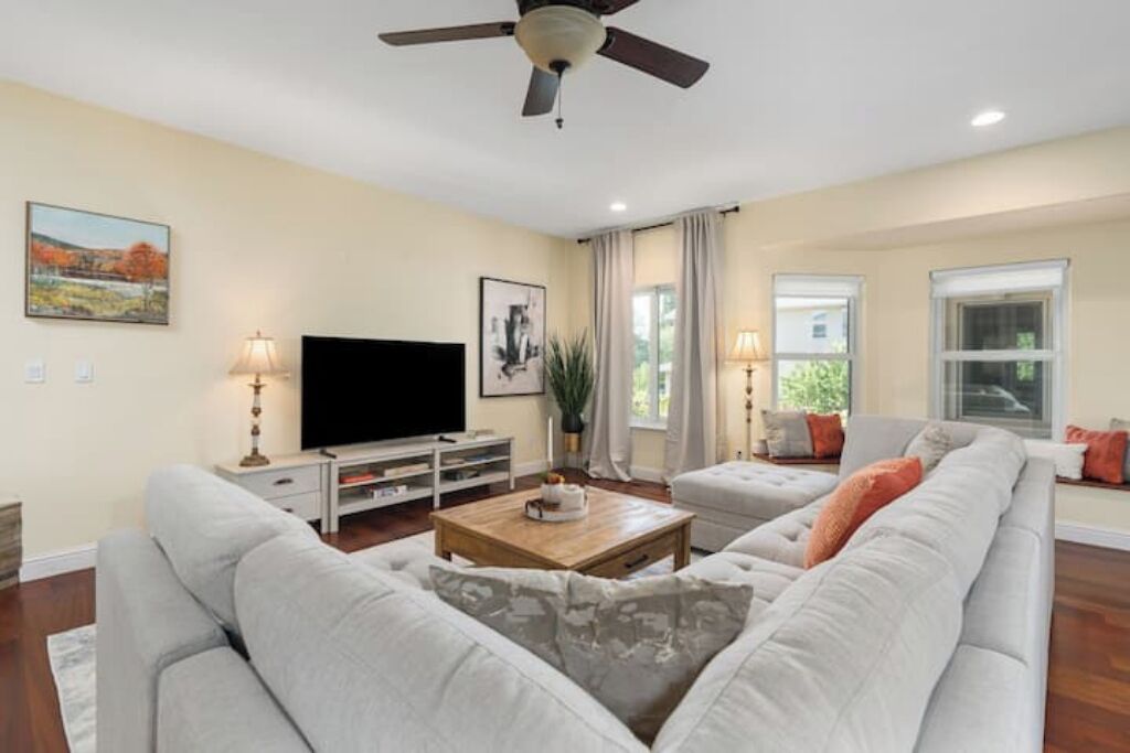 A living room with a flat-screen TV, a ceiling fan, a sofa, a coffee table, and a window with curtains.