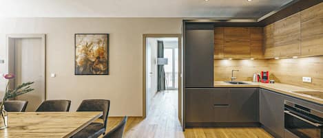 Una cocina moderna con armarios de madera, horno empotrado y comedor con mesa y sillas de madera.