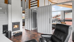 A modern living room with a fireplace, a black leather chair, and a view of the outside. - 2 bedroom amazing home in Aabenraa (Aabenraa)