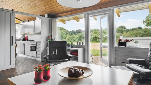 A modern kitchen with white cabinets, a dining area with a white table, and a view of a lush garden through large glass doors. - 2 bedroom amazing home in Aabenraa (Aabenraa)