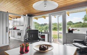 Une cuisine moderne avec des meubles blancs, un coin repas doté d’une table blanche, et une vue sur un jardin luxuriant grâce à de grandes portes vitrées.